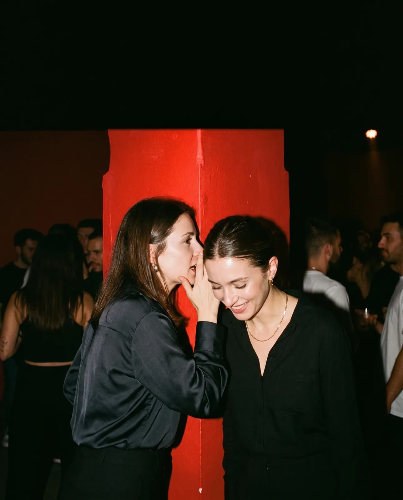 Campaign image: two women talking close, by a red pillar